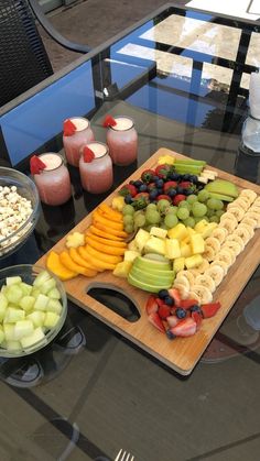 an assortment of fruits and snacks on a table with glasses of juice in the background