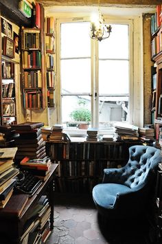 a room filled with lots of books and a blue chair in front of a window