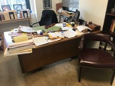 an office desk with many papers on it and a chair in front of the desk