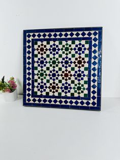 a blue and white tile wall hanging next to a potted plant on a table