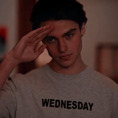 a young man holding his hand to his head and looking at the camera while wearing a wednesday t - shirt