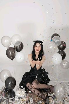 a woman sitting on the floor surrounded by balloons and confetti in front of her