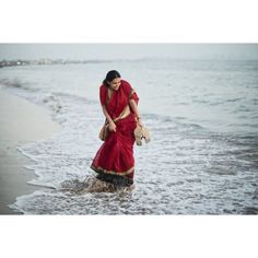 a woman in a red sari walking into the ocean