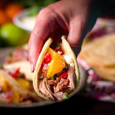 a hand holding a taco with meat and pineapple salsa on it next to some tortillas