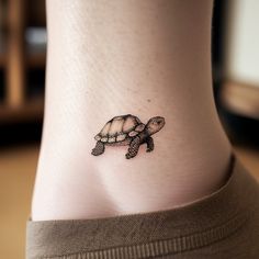 a small turtle tattoo on the side of a woman's leg, it is black and white