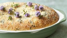 a close up of a cake in a white dish with purple flowers on the top