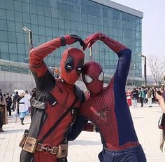 two people dressed as spider - man and deadpool pose for a photo in front of a crowd