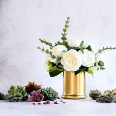 white flowers in a gold vase surrounded by succulents