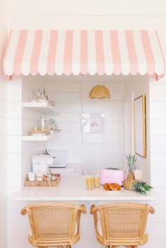 two chairs sitting under a pink and white awning next to a counter with pineapples on it