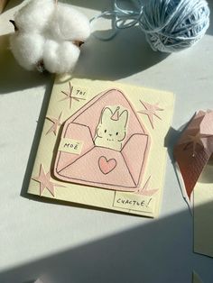 an envelope with a bunny inside is on the table next to some yarn and cotton