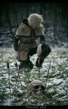 a man kneeling down in the snow next to a skull and some dead plants on the ground