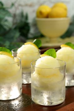 four glasses filled with ice cream and lemons on a table next to a bowl of lemons