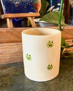 a plant in a pot with smiley faces painted on the side and green leaves sticking out of it