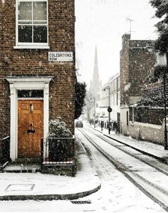 a snowy day in the city with snow falling on buildings and cars parked along the street