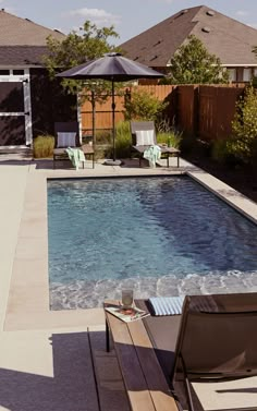 an empty swimming pool with lounge chairs and umbrellas around it, in the backyard