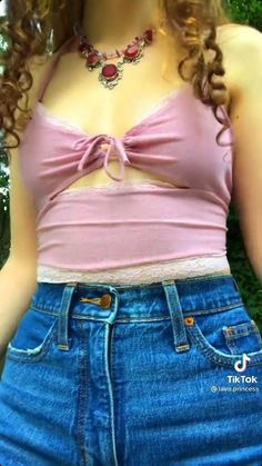 a woman with long curly hair wearing a pink top and blue jean shorts is posing for the camera