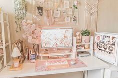 a white desk topped with a computer monitor next to a pink flower filled vase on top of it