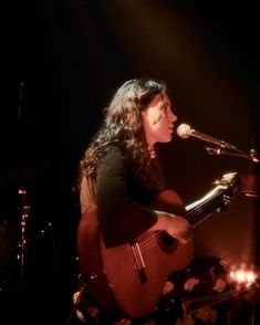 a woman sitting in front of a microphone while holding a guitar and singing into a microphone