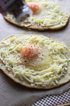 two flatbreads with cheese and an egg on top are being prepared to be eaten