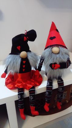 two stuffed gnomes sitting on top of a white table with red and black decorations