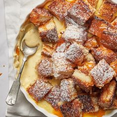 a bowl filled with french toast covered in powdered sugar next to a spoon and napkin