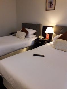 two beds in a hotel room with white linens and brown pillows, one has a remote control on the bed