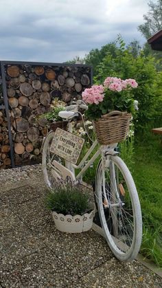 a bicycle with flowers in the basket is parked next to a firewood log rack