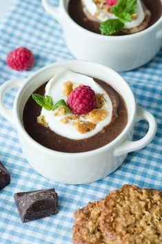 two white bowls filled with chocolate pudding and raspberries on a blue checkered table cloth