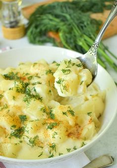 a spoon full of mashed potatoes with dill sprig on top and green onions in the background