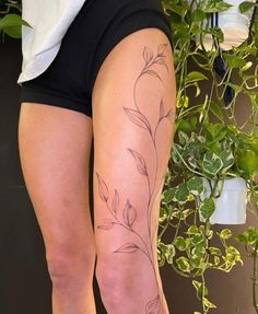 a woman's legs with tattoos on them and plants in the back ground behind her