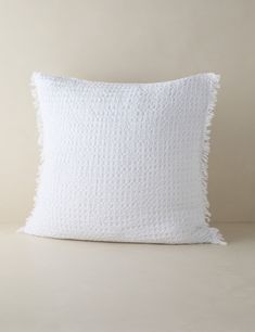 a white pillow with fraying on the front and back, sitting on a beige surface