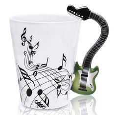 a coffee cup with a guitar handle and musical notes painted on the side, sitting next to a ceramic mug