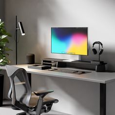 a desk with a computer monitor and headphones on it, next to a plant