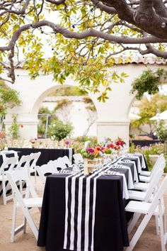 black and white striped tablecloths are set up for an outdoor wedding reception under a tree