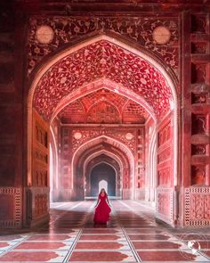 a woman in a long red dress is walking through an ornate building with arches and doorways