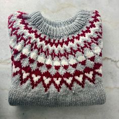 "A warm, chunky-knit pullover style sweater with a lovely geometric pattern around the yoke. It's a soft grey with white and burgundy/red. This sweater was worked bottom-up in the round to the underarm, the sleeves were worked separately, and then all parts were joined together on one needle to the yoke and neck opening. Likely a large, but please see details below. The measurements are taken while the sweater is laying flat. Measures:  20\" (51 cm) across shoulders (roughly, as the shoulders slope)  26\" (66 cm) across chest 31\" (78.75 cm) from front neck to hem 18\" (45.75 cm) from underarm to end of sleeve 52\" (132 cm) around at bottom hem" Cozy Fair Isle Pattern Sweater, White Scandinavian Sweater For Fall, White Scandinavian Style Sweater For Fall, White Scandinavian Style Fall Sweater, Cozy Gray Chunky Knit Pattern, Scandinavian Hand Knitted Crew Neck Sweater, Cozy Knit Sweater With Fair Isle Pattern, Cozy Gray Winter Knitting Pattern, White Nordic Sweater With Fair Isle Pattern