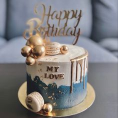 a birthday cake decorated with gold and blue icing is on a table next to a couch