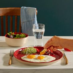 a person is cutting up an egg on a red plate next to a glass of water