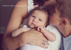 a woman holding a baby in her arms and kissing the man's face with his hand