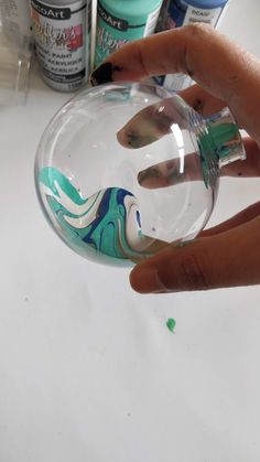 someone is holding a glass ball with some paint on it and there are other bottles in the background