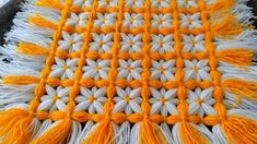 an orange and white crocheted blanket with tassels on top of it