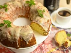 a bundt cake with icing and green leaves on it sitting on a plate next to a cup of coffee