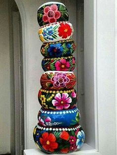 a tall stack of colorfully painted vases sitting on top of a white shelf