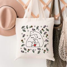 a white tote bag with a bear holding a heart on the front and flowers around it