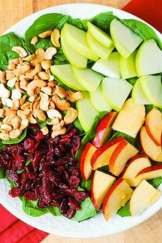 a white bowl filled with apples, cranberry sauce and nuts next to a red napkin