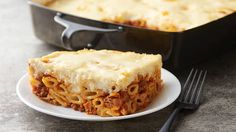 a white plate topped with lasagna next to a skillet filled with pasta