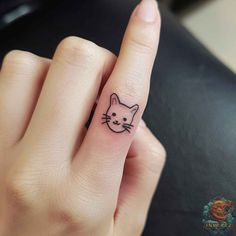 a person with a cat tattoo on their finger and the ring is in black ink