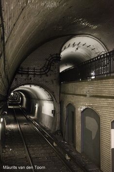 an underground subway tunnel with graffiti on the walls and rails leading to it's exit