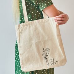 a woman holding a tote bag with flowers on it