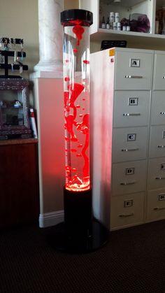 a tall tower with red liquid in it sitting on top of a floor next to filing cabinets